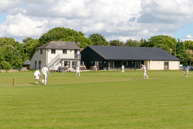 Wilbrahams' Memorial Hall with a cricket match underway in the foreground
