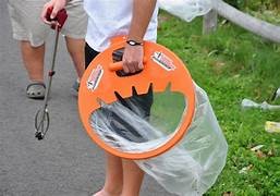 Image of a person's lower body holding a litter picker and plastic bag, littered grass in the background and the legs of a second person.